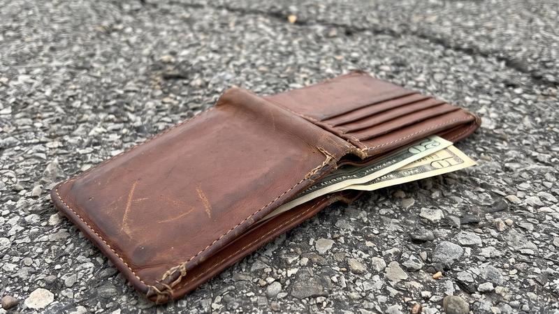A worn leather wallet lying on the asphalt of a store parking lot