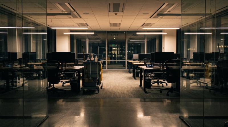 An empty modern office at night with a cleaning cart in the aisle between desks