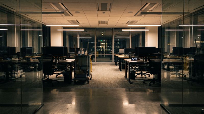 An empty modern office at night with a cleaning cart in the aisle between desks