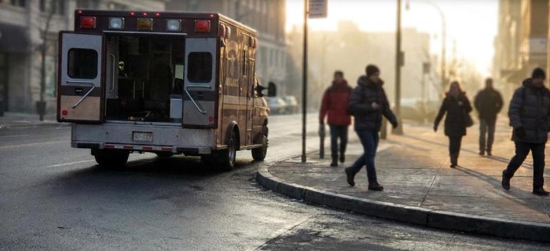 An ambulance with open doors parked on a city street in morning light