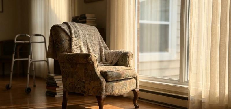An empty armchair by a bright window in a care home, soft afternoon light