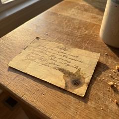 An old handwritten recipe index card, worn and stained, resting on a wooden kitchen table