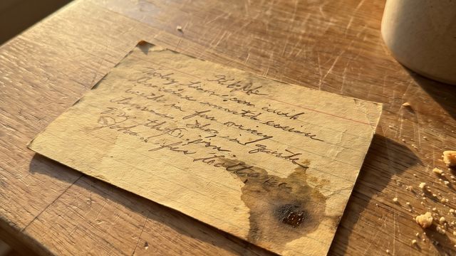 An old handwritten recipe index card, worn and stained, resting on a wooden kitchen table