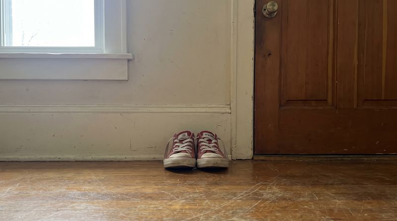 A small pair of children's shoes lined up perfectly straight against a wall by a door
