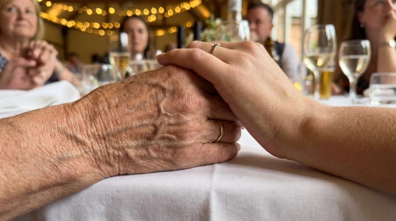 An older woman's hand and a younger woman's hand clasped together at a celebration