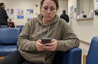 A woman sitting alone in a hospital waiting room, holding her phone