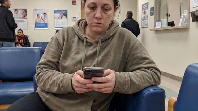 A woman sitting alone in a hospital waiting room, holding her phone