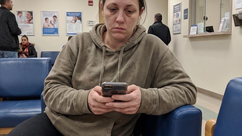 A woman sitting alone in a hospital waiting room, holding her phone