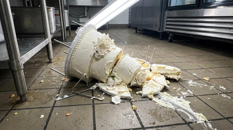 A toppled tiered wedding cake collapsed on a kitchen floor, broken tiers and smeared frosting