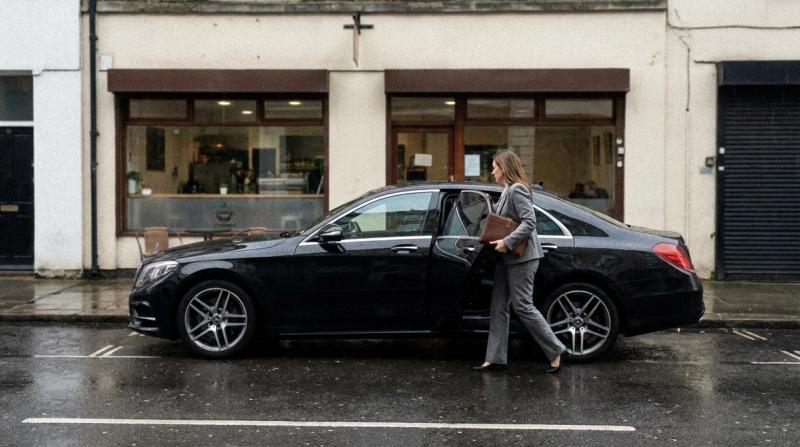 A black car parked outside a small café as a woman in a suit steps out holding a folder