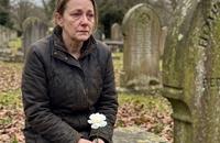 A mother sitting quietly on a stone bench in a peaceful cemetery