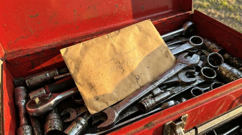 A yellowed envelope resting among old wrenches inside an open steel toolbox