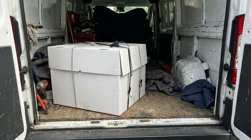 A white cake delivery box strapped in the back of a van, ready for delivery