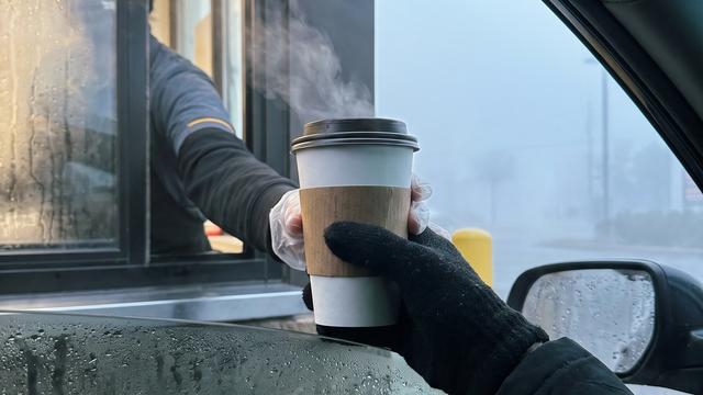 A paper coffee cup being passed from a drive-through window on an early foggy morning