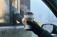 A paper coffee cup being passed from a drive-through window on an early foggy morning