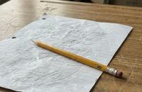 A worn yellow pencil resting on a crumpled sheet of lined paper on an old wooden school desk by a window