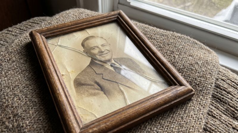 An old framed photograph of a man in a teacher's jacket, the frame slightly cracked