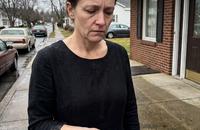 A woman standing alone outside a funeral home, holding a small key