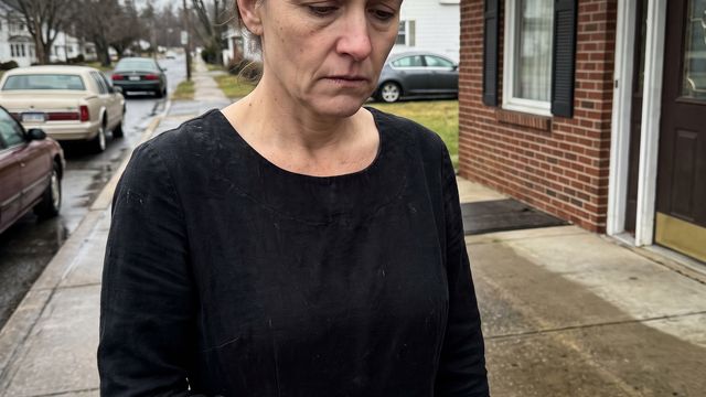 A woman standing alone outside a funeral home, holding a small key