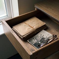 An open hospital bedside drawer holding a stack of unsent birthday cards and a creased photograph