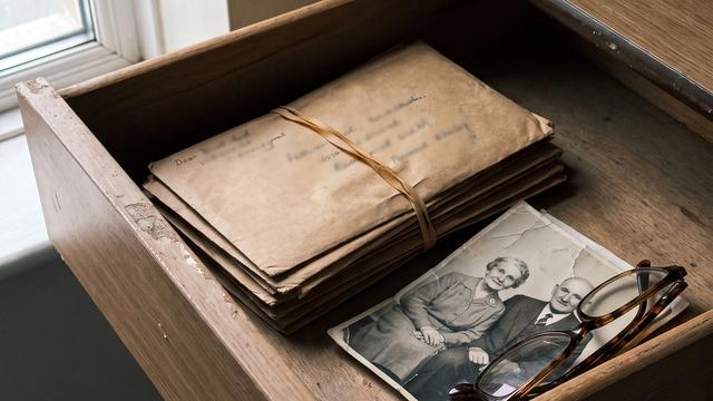 An open hospital bedside drawer holding a stack of unsent birthday cards and a creased photograph