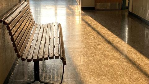 An empty school hallway in evening light with a wooden bench outside the front office
