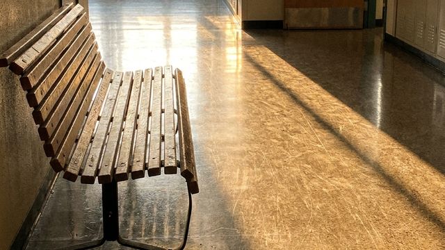 An empty school hallway in evening light with a wooden bench outside the front office