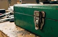 A worn green metal toolbox with a stuck latch sitting on a wooden garage workbench in warm light