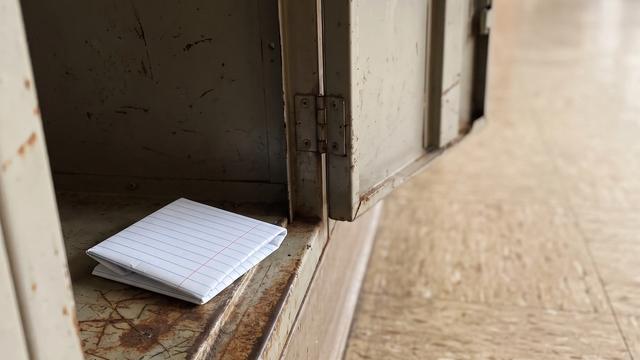 A small square of folded lined exercise paper resting inside an old metal school locker