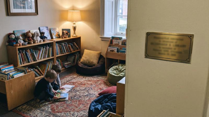 A cosy children's reading corner in a small library with low shelves and a small brass name plate on the wall
