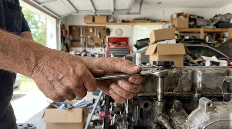 An older man's weathered hands tightening a bolt with a worn wrench in a home garage
