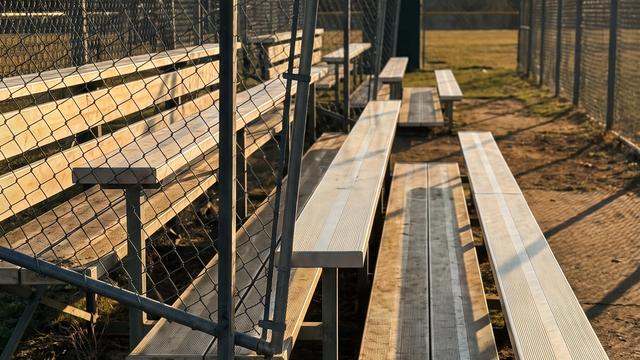 Empty metal bleachers at a high school baseball field in late afternoon light, one section in shadow