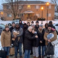 A crowd of neighbors gathering in the street outside an apartment building at dusk