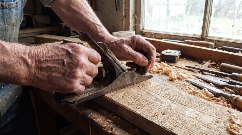 An older carpenter's weathered hands smoothing a piece of wood in a workshop