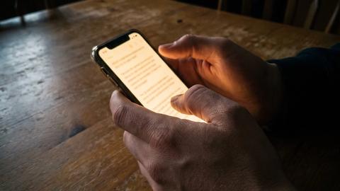 A phone screen glowing with a text conversation, held in a woman's hands at a kitchen table at night