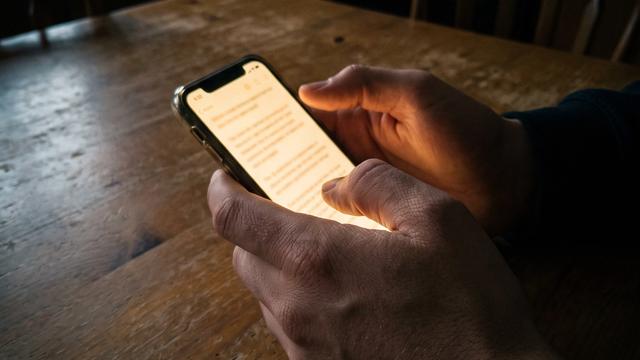 A phone screen glowing with a text conversation, held in a woman's hands at a kitchen table at night