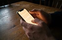 A phone screen glowing with a text conversation, held in a woman's hands at a kitchen table at night