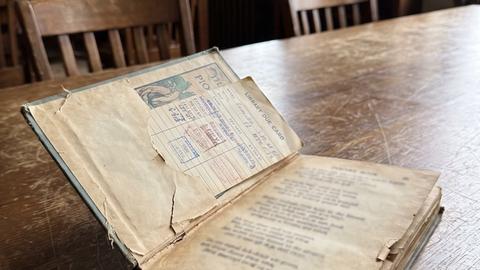 An old battered poetry book with a yellowed library card in its sleeve, resting on a wooden library desk