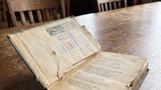 An old battered poetry book with a yellowed library card in its sleeve, resting on a wooden library desk