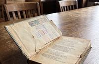 An old battered poetry book with a yellowed library card in its sleeve, resting on a wooden library desk