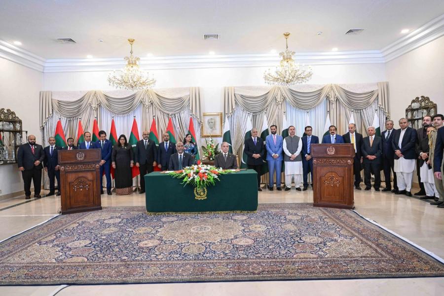 A wide view of the hall with both delegations standing in a line behind two lecterns and a green signing table.