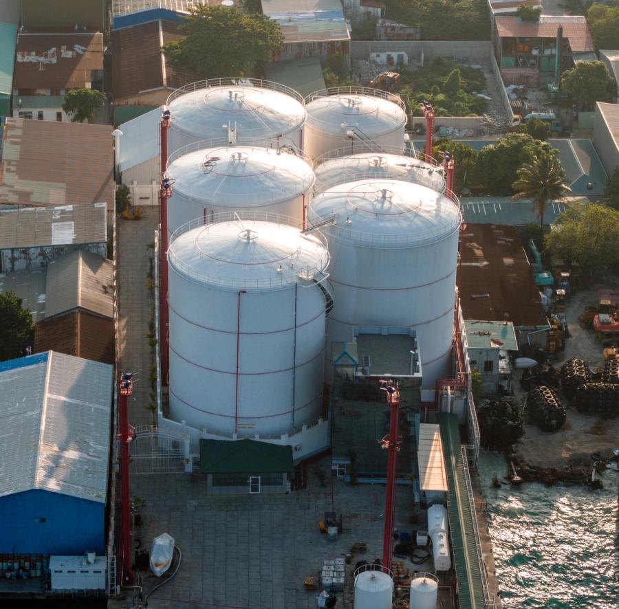 Aerial view of six white cylindrical fuel tanks beside a quay, surrounded by industrial buildings