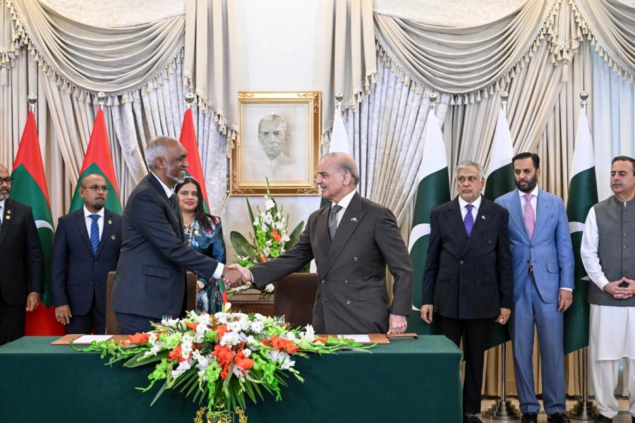 President Muizzu and Prime Minister Sharif shake hands in front of Maldivian and Pakistani flags, with both delegations standing behind them.