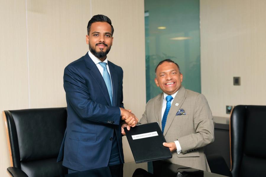 Two men in suits shake hands while holding a document folder between them