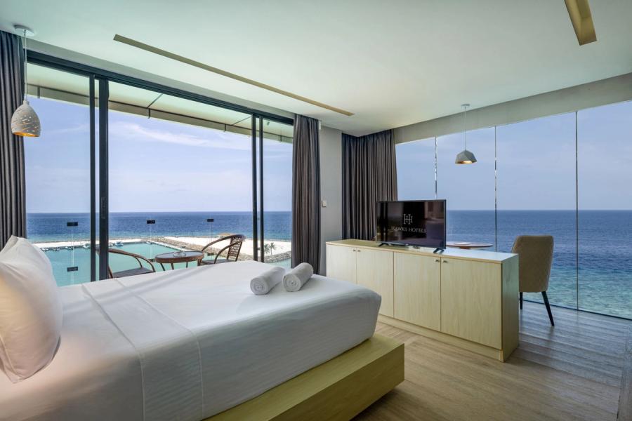 A hotel bedroom with floor-to-ceiling windows overlooking a pool and the sea
