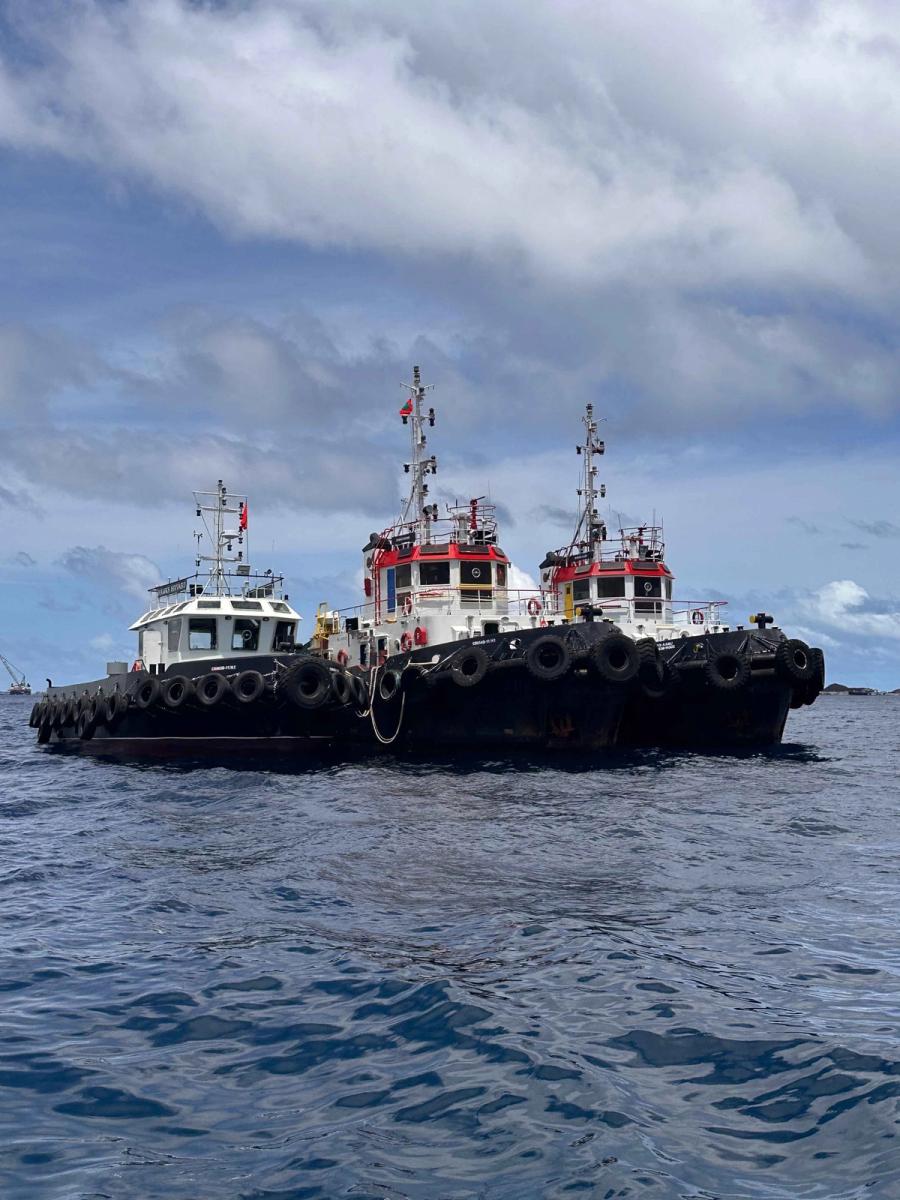 Three tugboats with tyre fenders moored together on open water under a cloudy sky