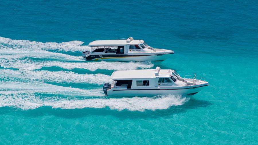 Two white speedboats running side by side across turquoise water, seen from above