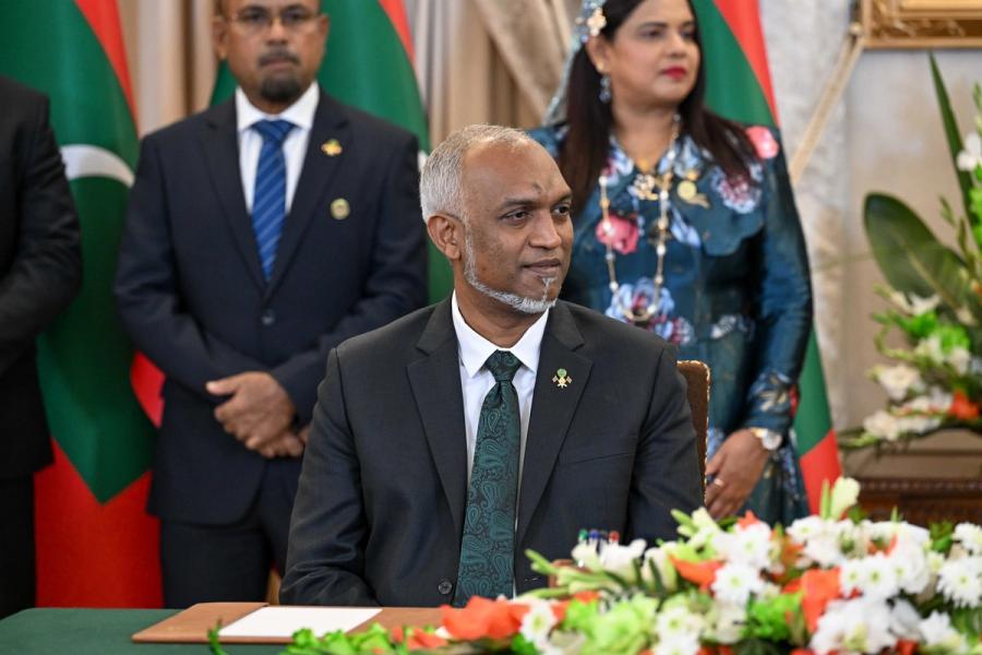 President Muizzu seated at the signing table behind a flower arrangement, with Maldivian officials standing behind him.