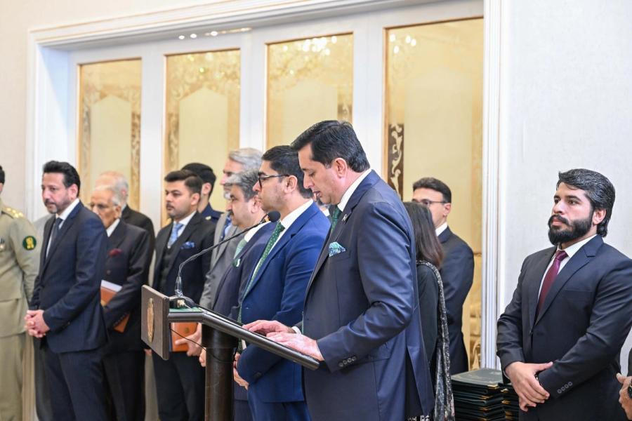 Pakistani officials stand at a lectern at the side of the hall as the agreements are announced.