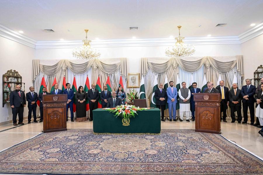 A wide view of a reception hall with two lecterns, a green signing table and both delegations lined up under chandeliers.
